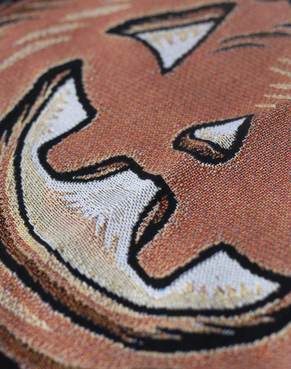 Close-up of a woven textile featuring a  jack-o-lantern face in orange-brown, cream, black, and tan tones.
